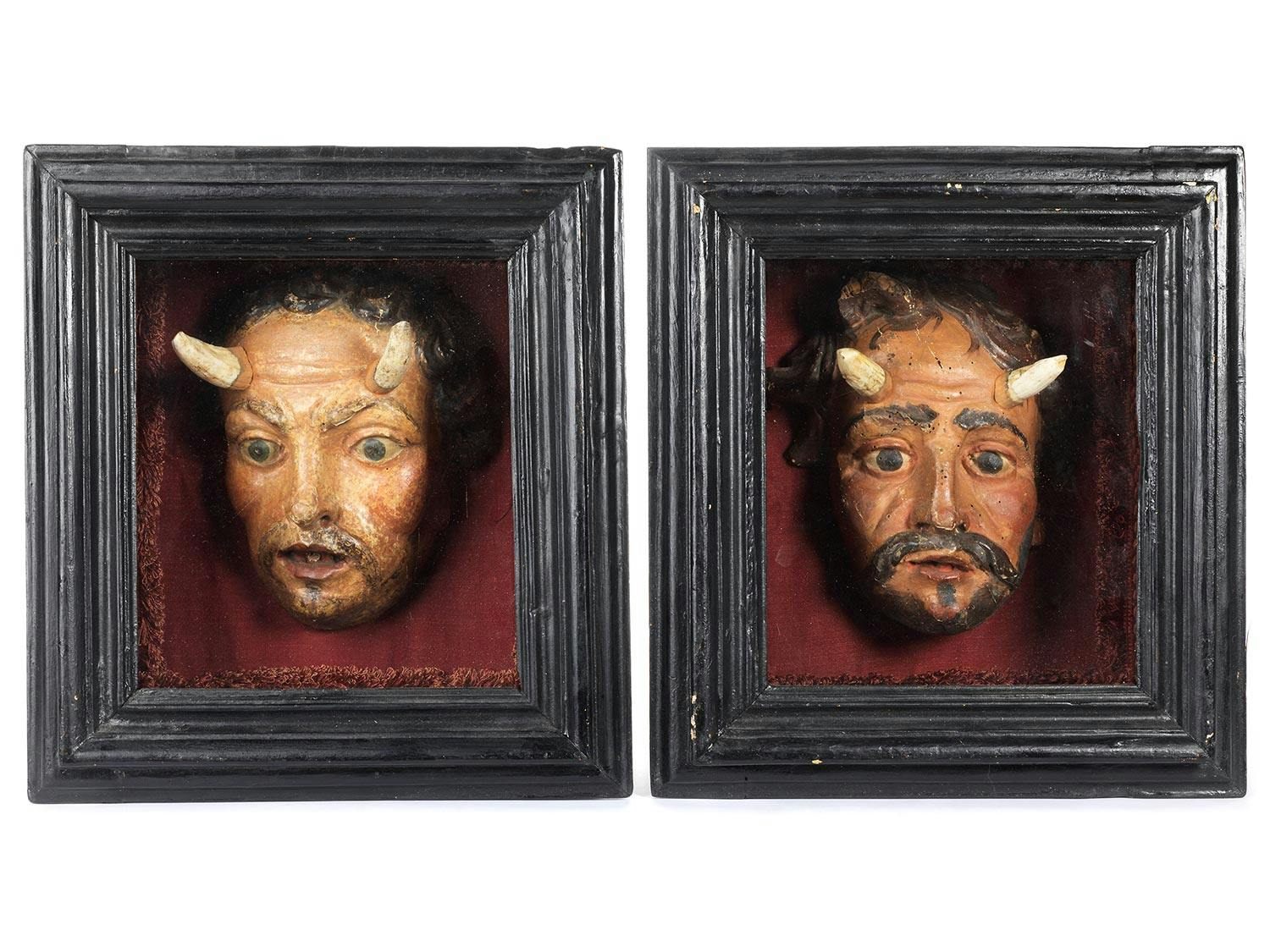 Zwei bemalte Holzskulpturen, die jeweils Gesichter eines Teufels mit Hörnern aus Hirschgeweih zeigen