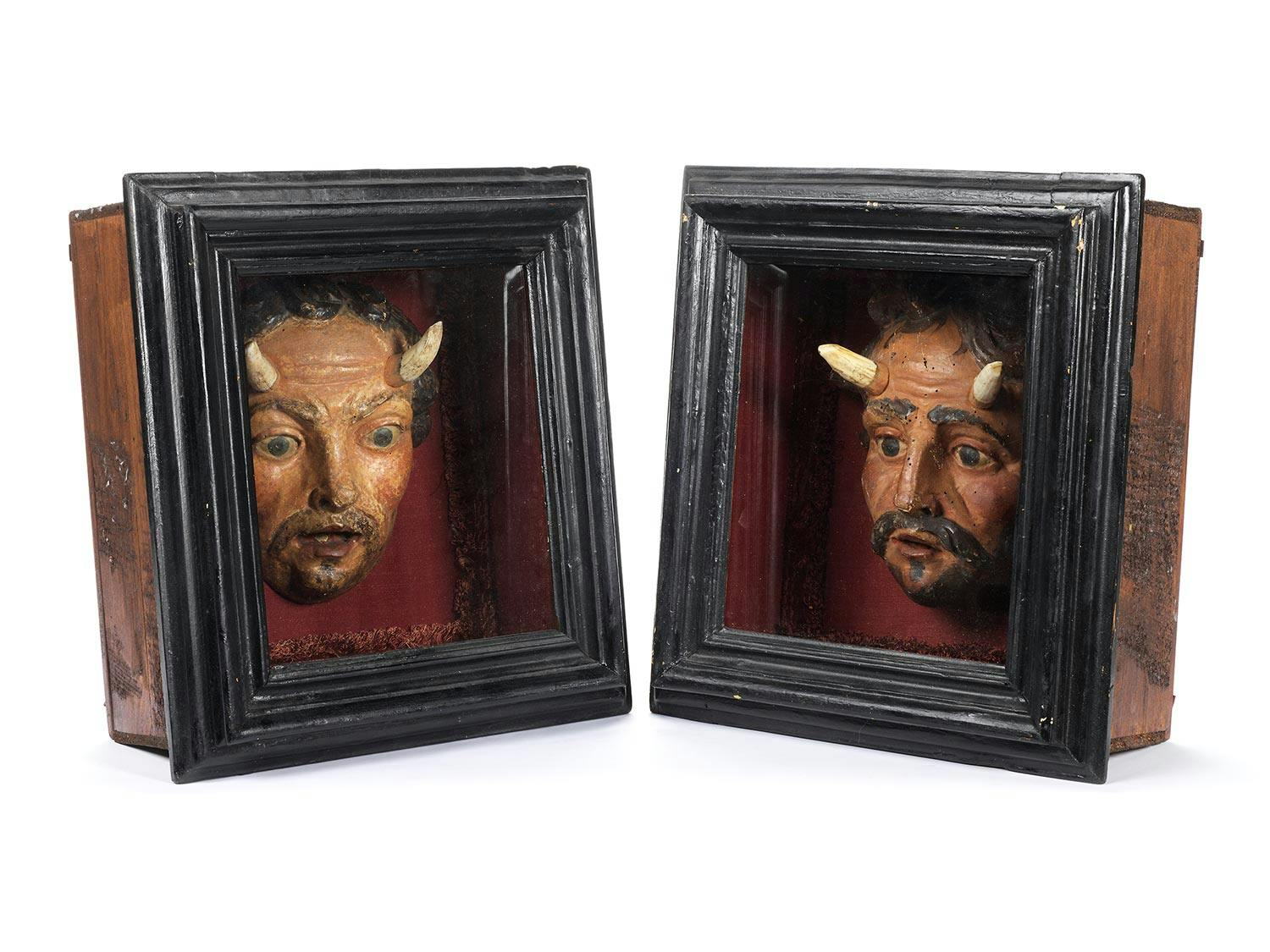Detailabbildung: Zwei bemalte Holzskulpturen, die jeweils Gesichter eines Teufels mit Hörnern aus Hirschgeweih zeigen